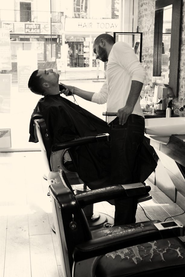A barber trimming a beard in a vintage chair at George's Barber Room, Kentish Town Road outside